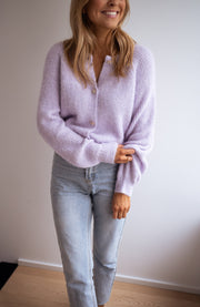 Gilet à boutons fleuris brillants porté par une femme, vue de trois-quarts, jean clair, mur blanc