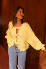 Gilet à liens noués jaune porté par une femme, vue de face, mur en bois, jean