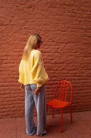 Gilet à liens noués jaune porté par une femme, silhouette entière, chaise orange, mur de briques
