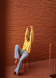 Gilet à liens noués jaune porté par une femme, vue de face, bras levés, chaise orange