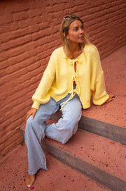 Gilet à liens noués jaune porté par une femme, assise, escalier, jean
