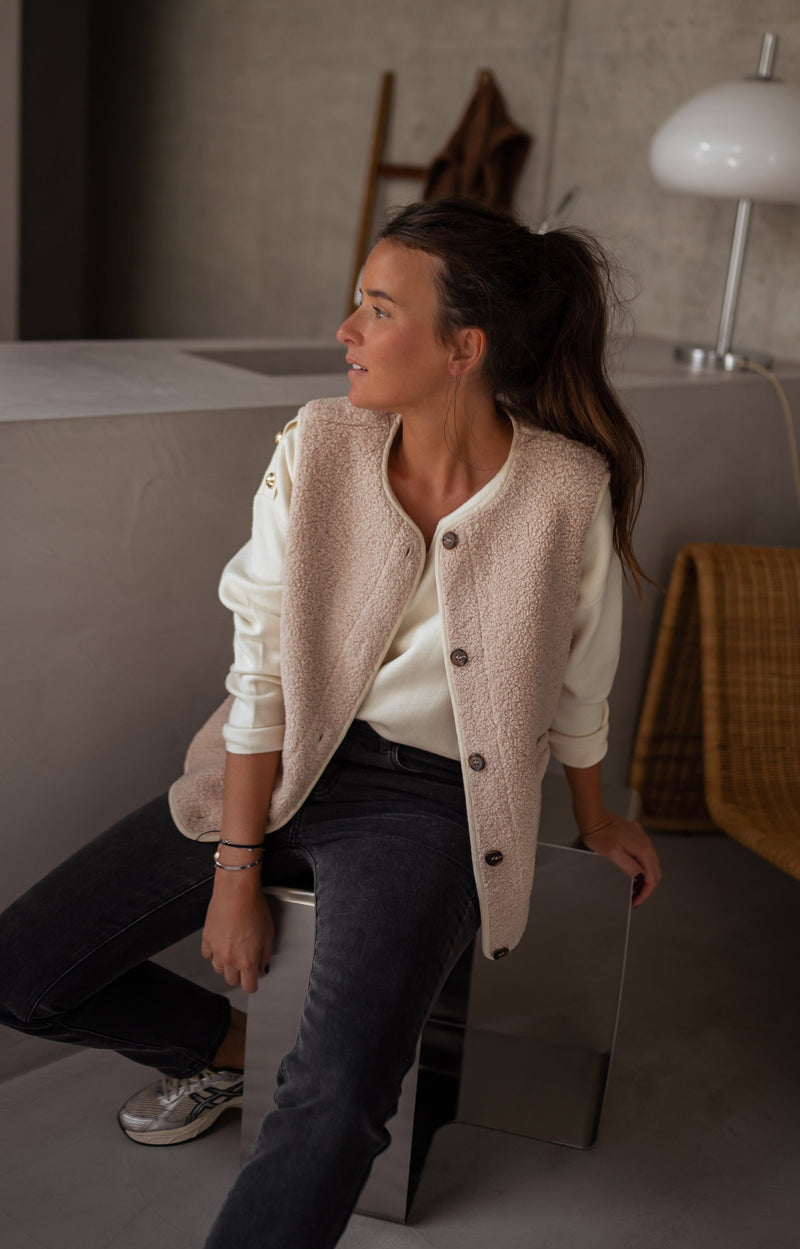 Gilet sans manches effet moumoute porté par une femme, vue de trois-quarts, gilet beige, haut crème, jean noir