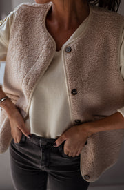 Gilet sans manches effet moumoute porté par une femme, vue rapprochée, boutons, haut crème