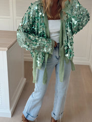 Gilet cache-cœur à paillettes porté par une femme, vue de face, placard blanc, veste ouverte