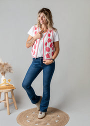 Gilet brodé floral sans manches porté par une femme, silhouette entière, fond gris, tabouret