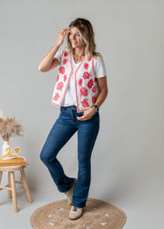 Gilet brodé floral sans manches porté par une femme, silhouette entière, main sur le gilet, tabouret