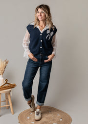 Ensemble gilet et chemise dentelle porté par une femme, silhouette entière, jean, tabouret