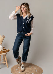 Ensemble gilet et chemise dentelle porté par une femme, silhouette entière, main sur la tête, jean