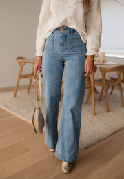 Jean évasé à deux boutons porté par une femme, vue rapprochée, jambes larges, sac