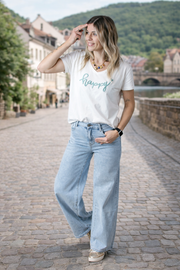 Jean large taille haute stretch porté par une femme, silhouette entière, rue pavée, t-shirt blanc