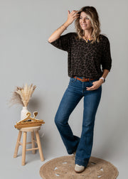 Jean flare en denim stretch porté par une femme, vue de trois-quarts, main sur la tête, haut noir