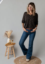 Jean flare en denim stretch porté par une femme, silhouette entière, haut noir, tabouret