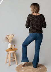 Jean flare en denim stretch porté par une femme, vue de dos, haut noir, tabouret
