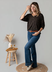 Jean flare en denim stretch porté par une femme, vue de trois-quarts, haut noir, tabouret