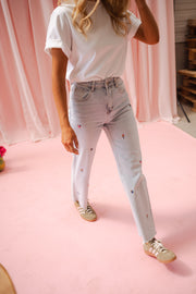 Jeans fleuri taille haute porté par une femme, vue de profil, sol rose, baskets