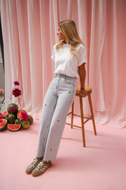 Jeans fleuri taille haute porté par une femme, vue de trois-quarts, tabouret, t-shirt blanc