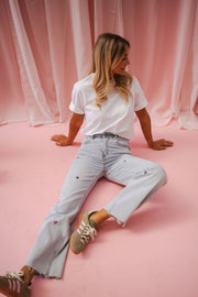Jeans fleuri taille haute porté par une femme, assise sur le sol rose, jambes allongées