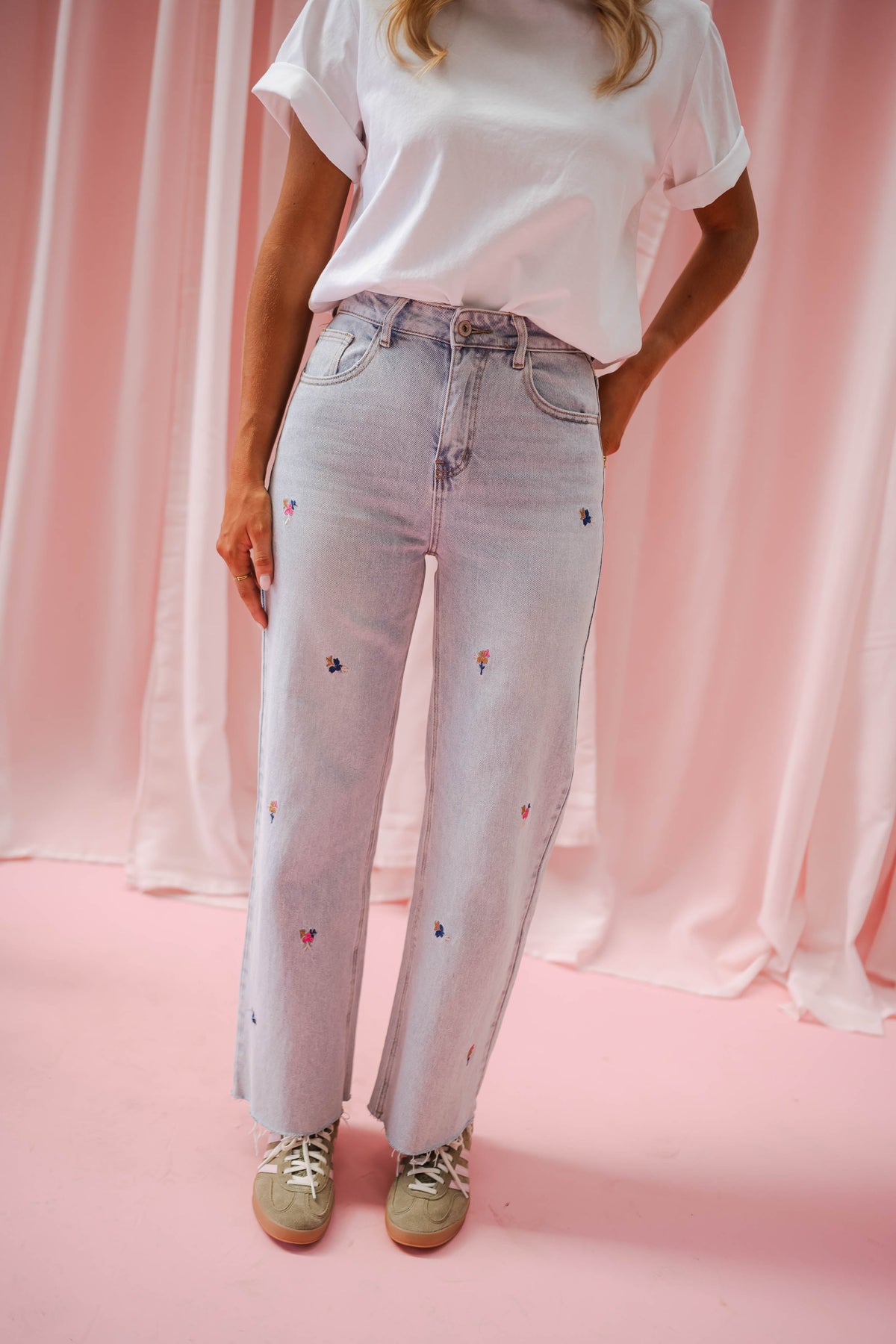 Jeans fleuri taille haute porté par une femme, silhouette entière, rideaux roses, t-shirt blanc