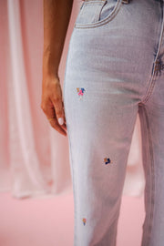 Jeans fleuri taille haute porté par une femme, vue rapprochée, fleurs brodées, jambe