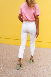 Jean taille haute effiloché blanc porté par une femme, silhouette entière, mur jaune, t-shirt rose