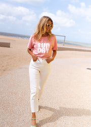 Jean taille haute effiloché blanc porté par une femme, silhouette entière, sable, ciel bleu