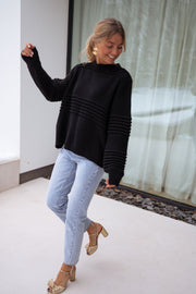 Jean droit légèrement court porté par une femme, silhouette entière, pull noir, sandales