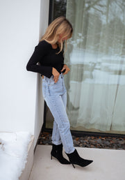 Jean droit légèrement court porté par une femme, vue de profil, pull noir, bottines noires