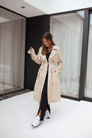 Trench ample ceinturé à poches porté par une femme, silhouette entière, main dans la poche