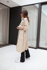 Trench ample ceinturé à poches porté par une femme, vue de profil, bottines noires