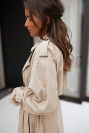 Trench ample ceinturé à poches porté par une femme, vue de profil, cheveux attachés, col relevé