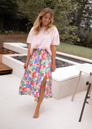 Jupe longue fleurie fendue portée par une femme, silhouette entière, pull rose, pieds nus