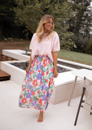 Jupe longue fleurie fendue portée par une femme, vue de trois-quarts, pull rose, sourire