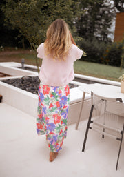 Jupe longue fleurie fendue portée par une femme, silhouette entière, pull rose, banc blanc