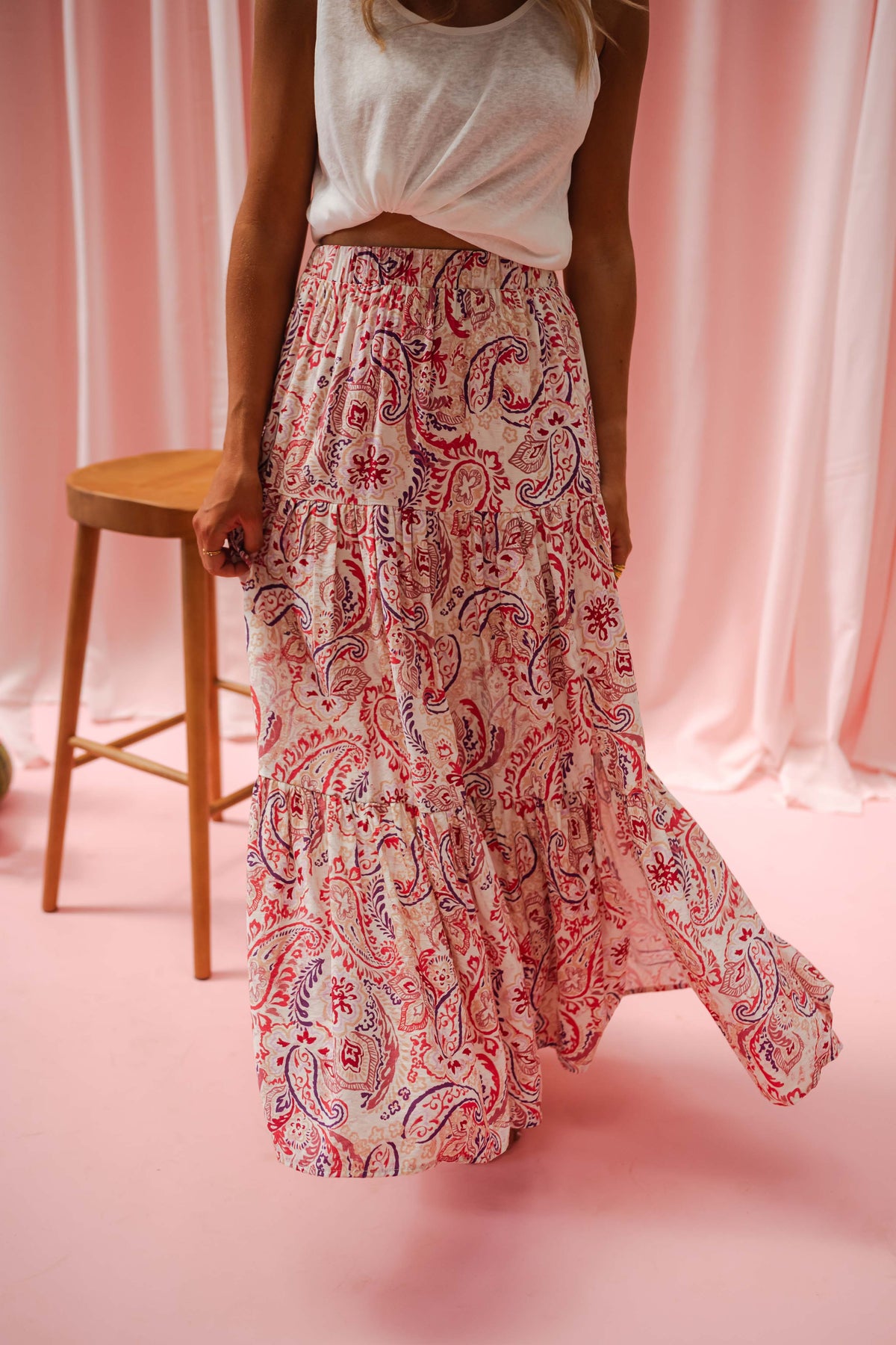 Jupe longue fluide à motifs portée par une femme, en marchant, rideaux roses, tabouret, jupe fleurie
