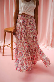 Jupe longue fluide à motifs portée par une femme, en marchant, rideaux roses, tabouret, jupe fleurie