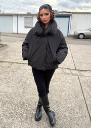 Veste courte noire col montant — vue portée en pied, en extérieur, pantalon noir et bottes épaisses