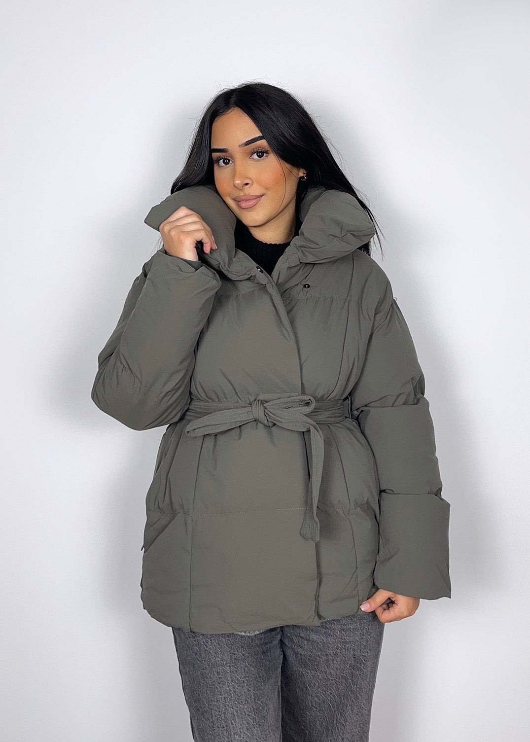Veste d’hiver courte grise — vue portée de face, col haut et ceinture nouée, mains près du col