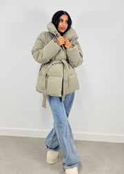 Veste d’hiver courte taupe — vue portée en pied en intérieur, jean évasé clair et bottes beiges