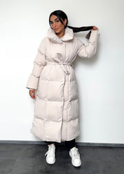Veste longue beige à ceinture — vue portée en pied, col montant et ceinture nouée, baskets blanches