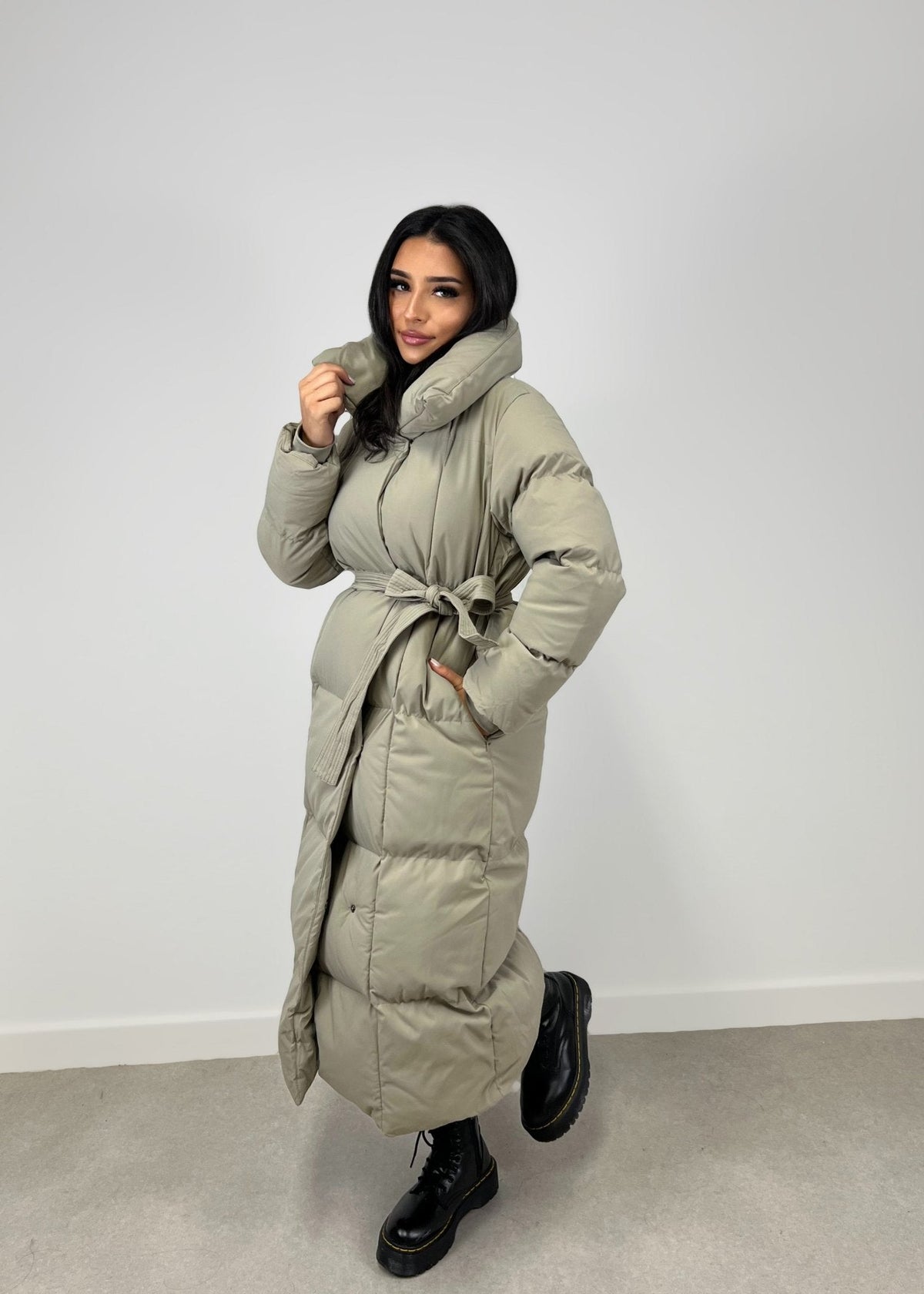 Veste longue taupe à ceinture — vue portée de profil en pied, fermée et ceinturée, bottines noires