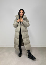 Veste longue taupe à ceinture — vue portée en pied, ouverte, bords tenus à deux mains