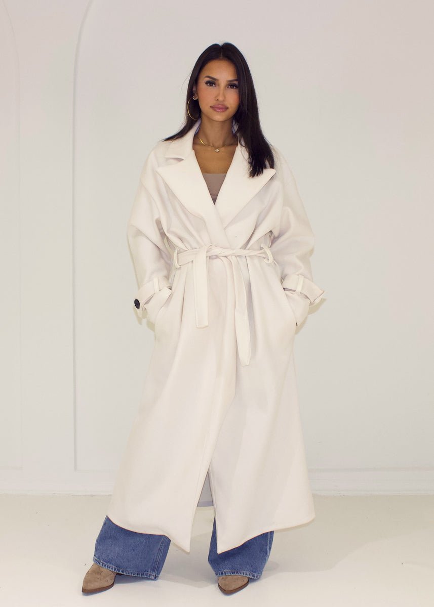 Manteau long écru à ceinture — vue de face, ceinture nouée.