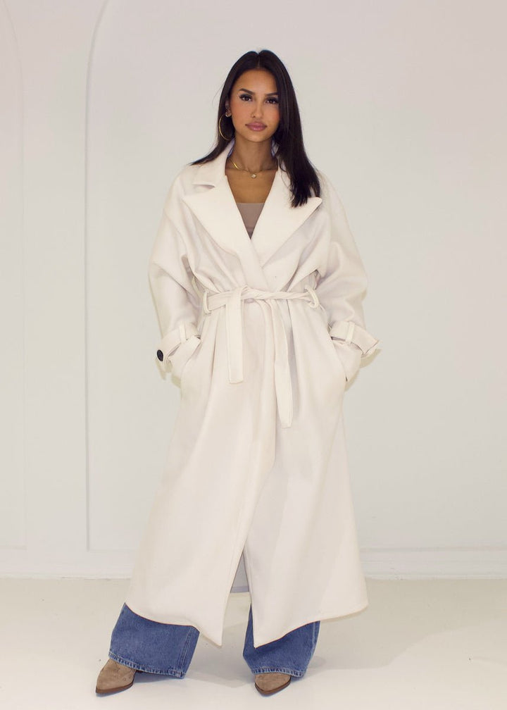 Manteau long écru à ceinture — vue de face, ceinture nouée.