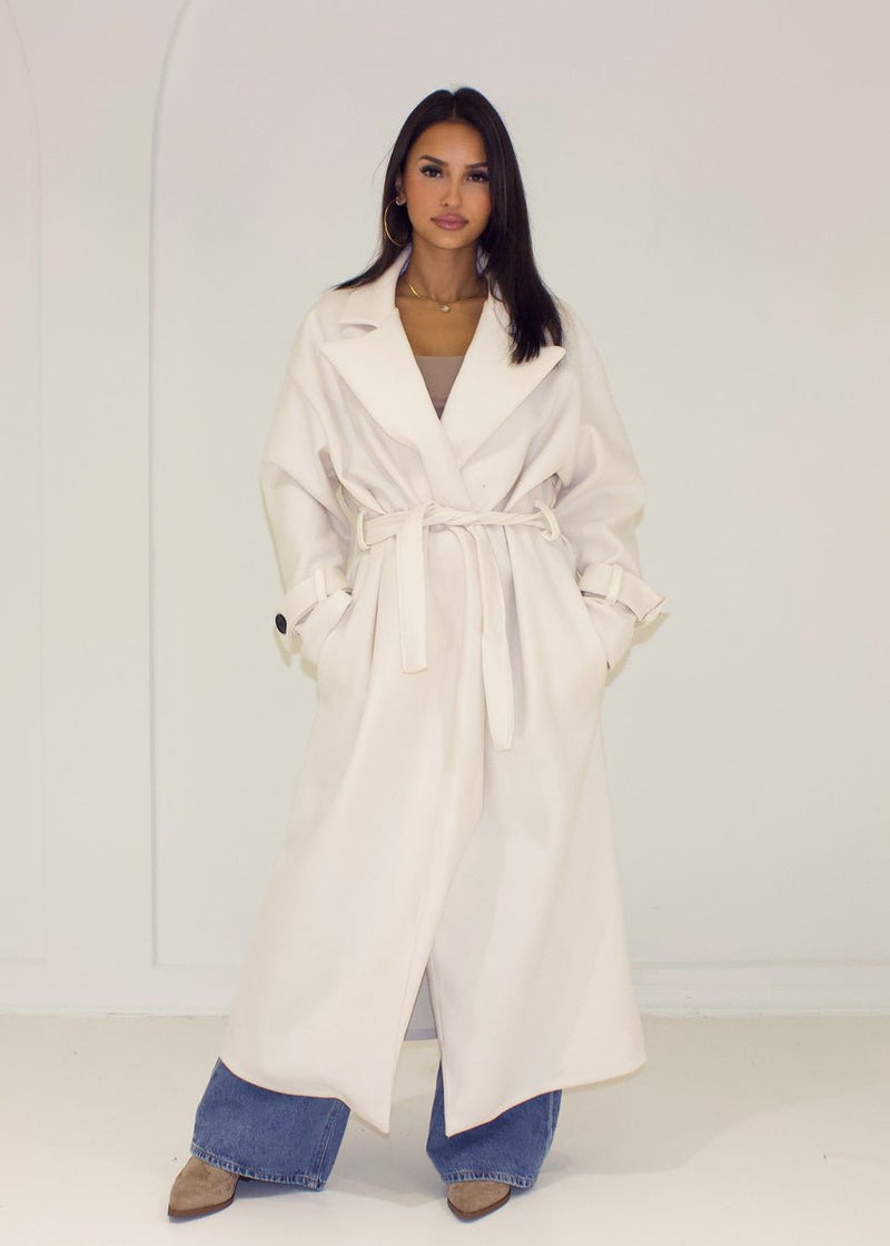 Manteau long écru à ceinture — vue de face, ceinture nouée.