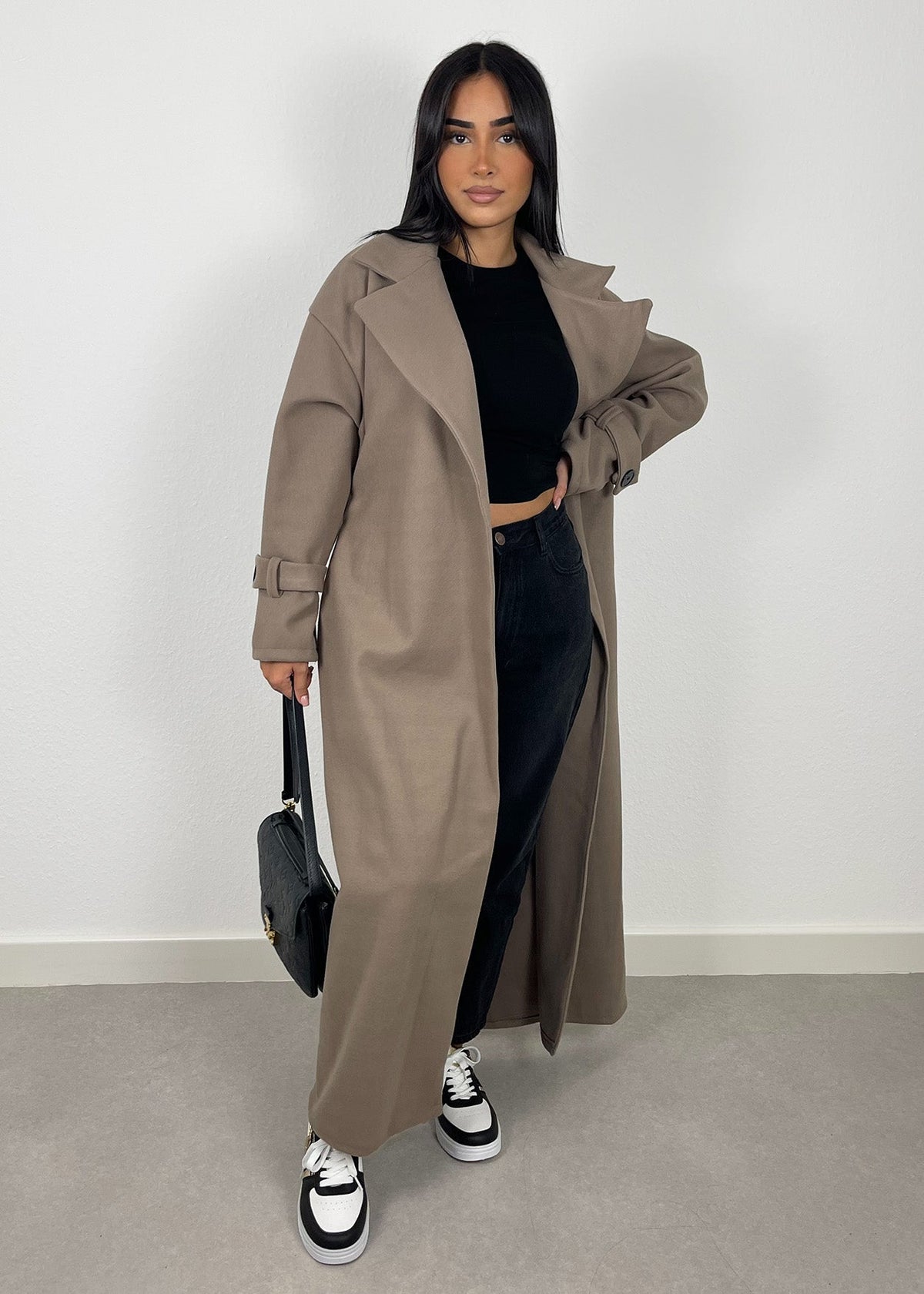 Manteau long taupe foncé — vue portée en pied, très long, haut et pantalon noirs, petit sac noir et baskets