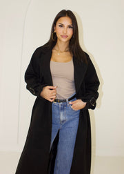 Trench long noir à ceinture — vue portée en pied, ouvert, haut beige et jean large