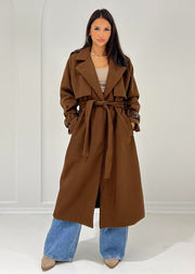 Trench long brun à ceinture — vue portée en pied, ouvert, légèrement de trois-quarts, haut beige et jean clair