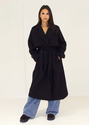 Trench long noir à ceinture — vue portée en pied, ceinturé