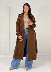 Trench long brun à ceinture — vue portée en pied, mains à la taille