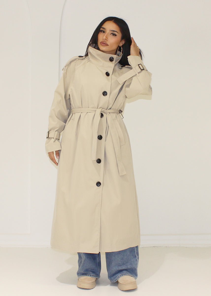 Trench long beige — vue portée en pied, ceinturé, jean large bleu